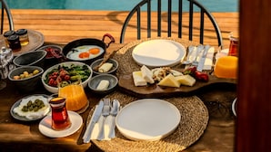 Desayuno dispuesto junto a una piscina, con diferentes platos, utensilios y un vaso de jugo de naranja.