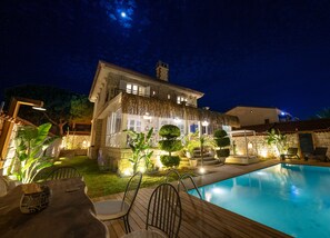 Une maison à deux étages avec une piscine, des murs en pierre et un toit de chaume.