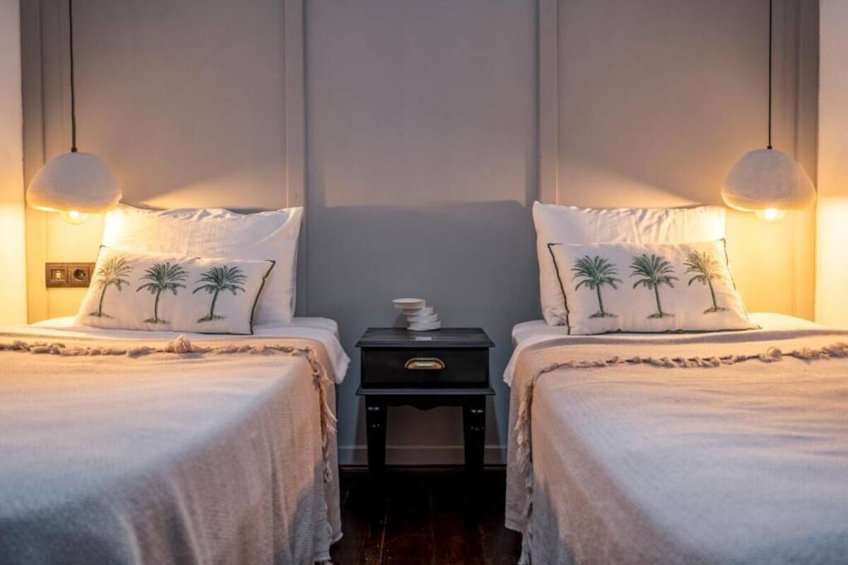 Una habitación con dos camas, cada una con un cojín con diseños de palmeras, una mesita de noche con lámpara y una lámpara de pared.
