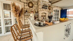 Una zona de bar con paredes de piedra, sillas de mimbre, una barra con una cúpula de vidrio y un letrero que dice "LIQUID THERAPY".