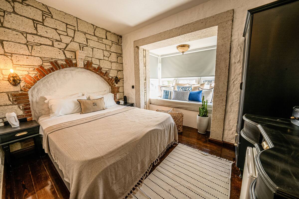 Un dormitorio con pared de piedra, una cama con cabecera blanca, una mesita de noche y un televisor sobre un mueble.
