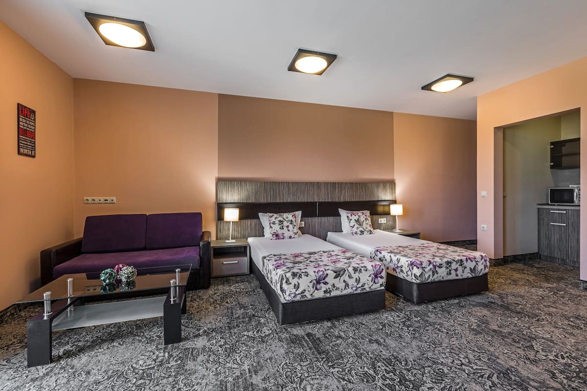 A hotel room with two beds, a sofa, a coffee table, and a kitchenette.