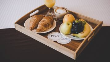 Uma bandeja de madeira com croissants, um copo de suco de laranja, uma xícara de café e um prato com uma maçã, uvas e uma banana.