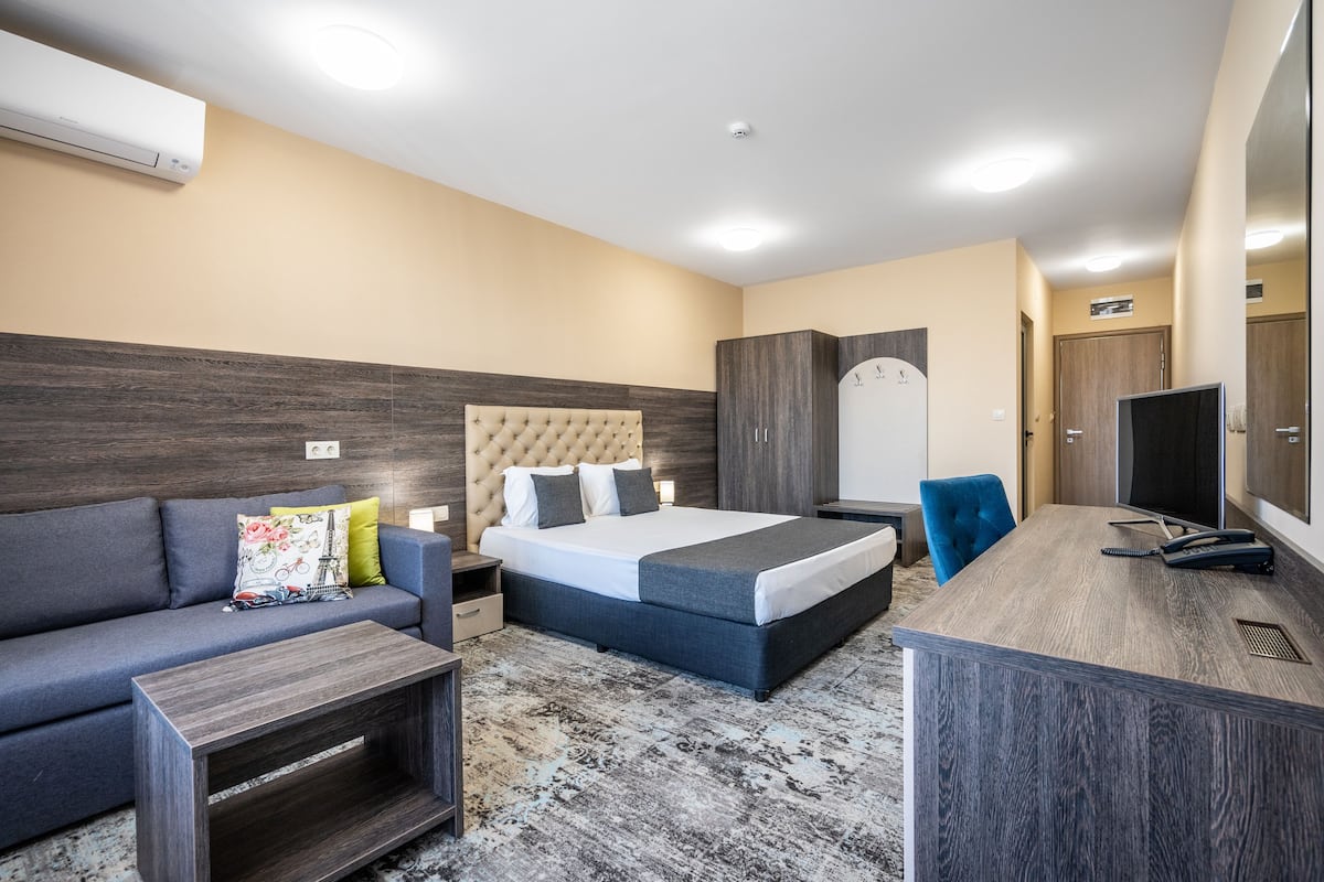 A modern hotel room with a bed, a sofa, a desk, and a wardrobe.