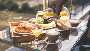 A breakfast tray with croissants, a glass of orange juice, a glass of milk, a plate of fruit, and a cup of coffee on a table by a window.