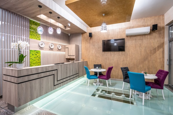 A modern reception area with a wooden reception desk, a flat-screen TV, and a seating area with colorful chairs. - Plaza Hotel (Plovdiv)