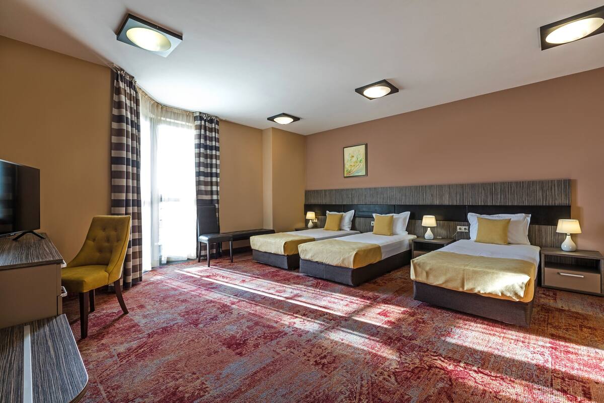 A hotel room with two beds, a desk, a chair, and a television.