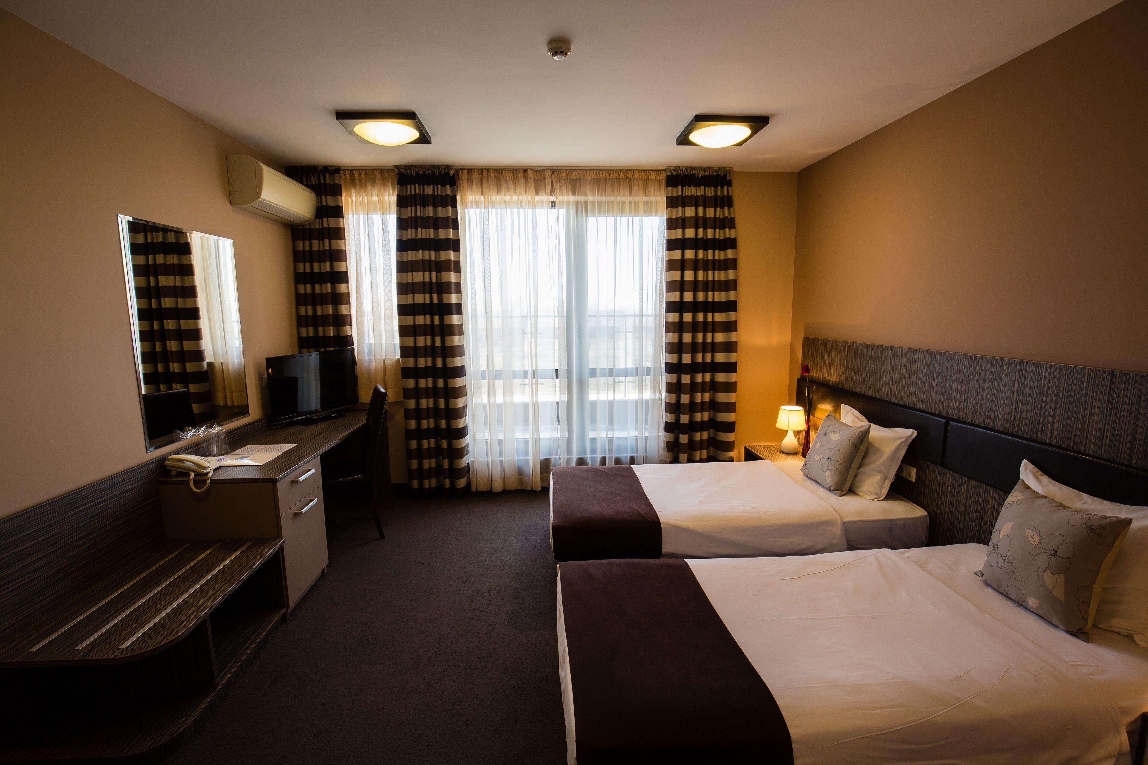 A hotel room with two beds, a desk, a chair, a mirror, and a window with curtains.