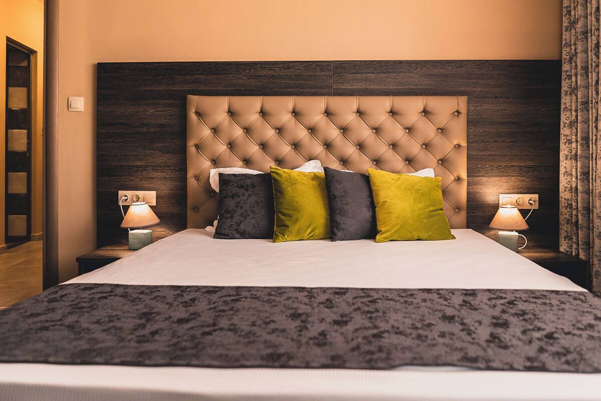 A neatly made bed with a tufted headboard, two bedside lamps, and a patterned throw blanket.