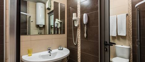 A bathroom with a sink, mirror, toilet, and shower.