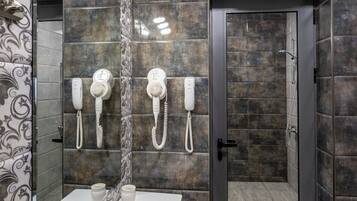 A modern bathroom with a large mirror, two hair dryers, a sink with a faucet, and a shower door.
