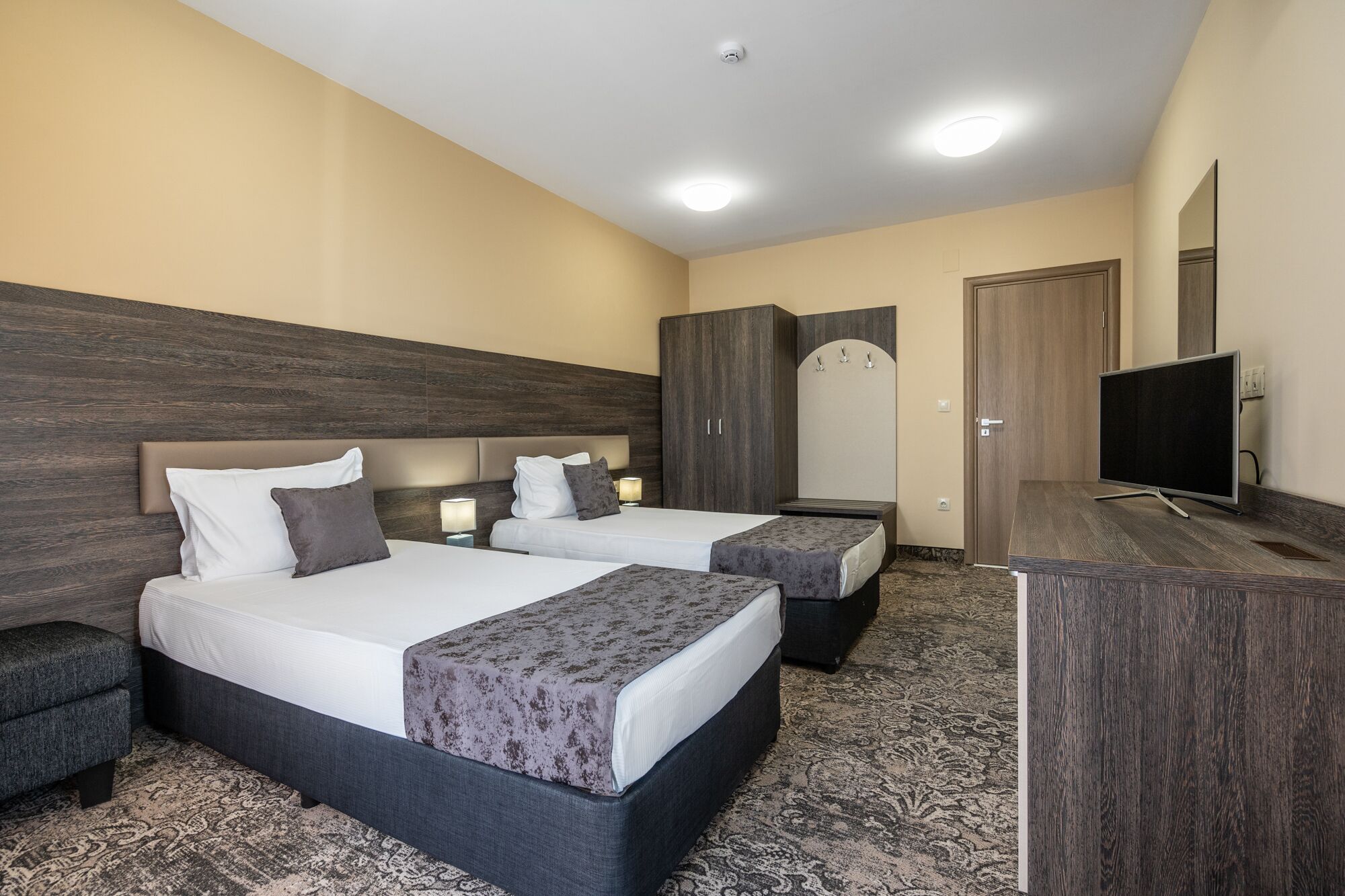 A hotel room with two beds, a desk, a TV, and a wardrobe.