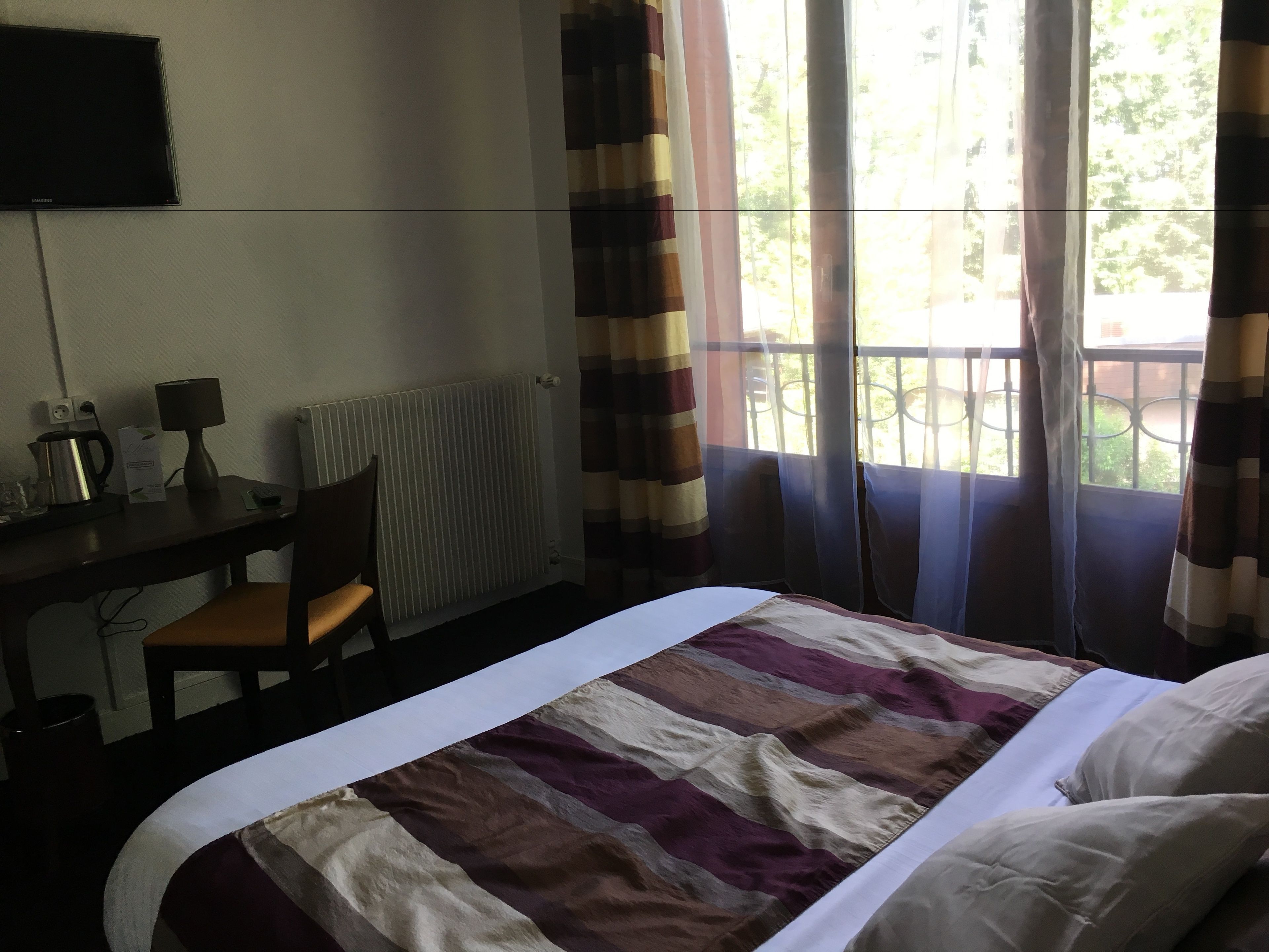 Une chambre d’hôtel comprenant un lit, un bureau avec une chaise, une lampe, une bouilloire et un radiateur.