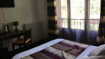 Une chambre d’hôtel comprenant un lit, un bureau avec une chaise, une lampe, une bouilloire et un radiateur.