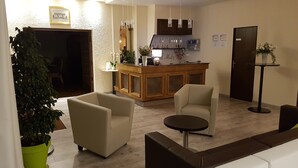 Un área de recepción con un mostrador de madera, dos sillones, una mesita y una planta en maceta.