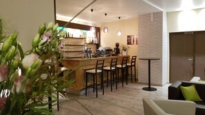 Zona de bar con mostrador, taburetes y máquina de café. Hay un área de estar con sofá y mesa.