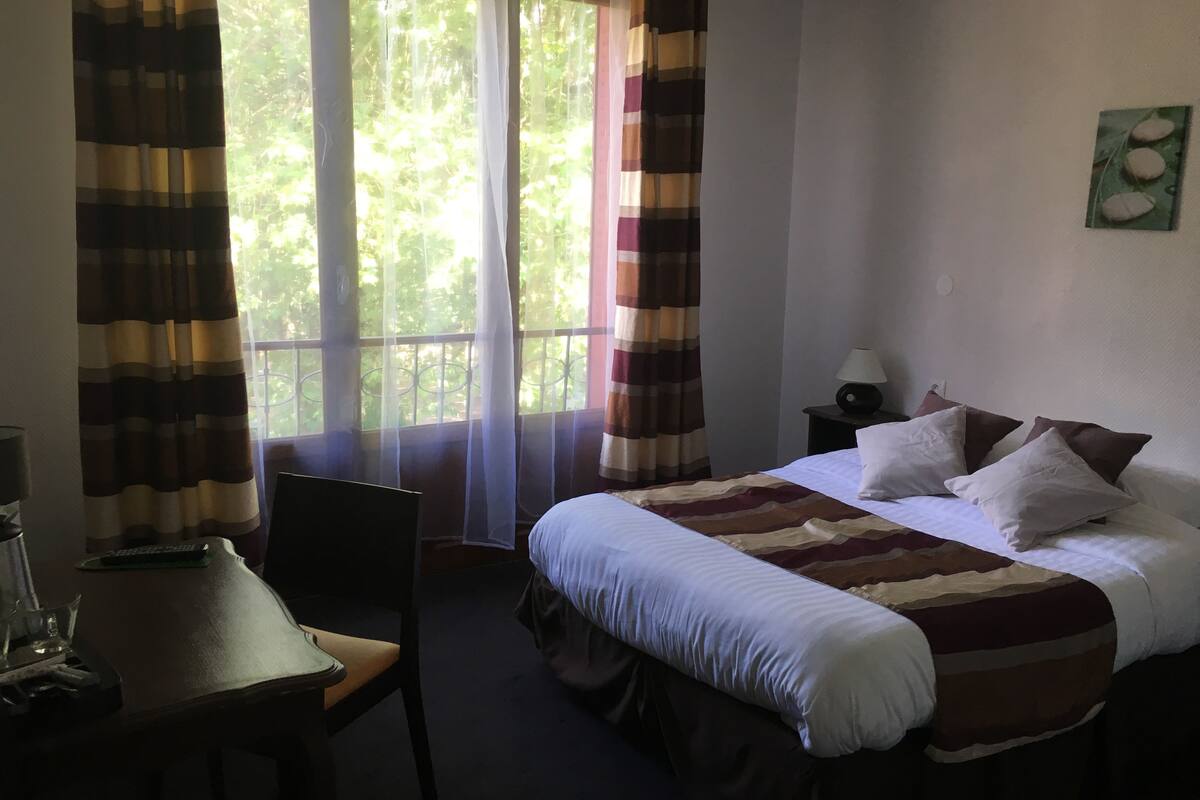 Una habitación de hotel con cama, una silla, una mesa y un ventanal con cortinas.