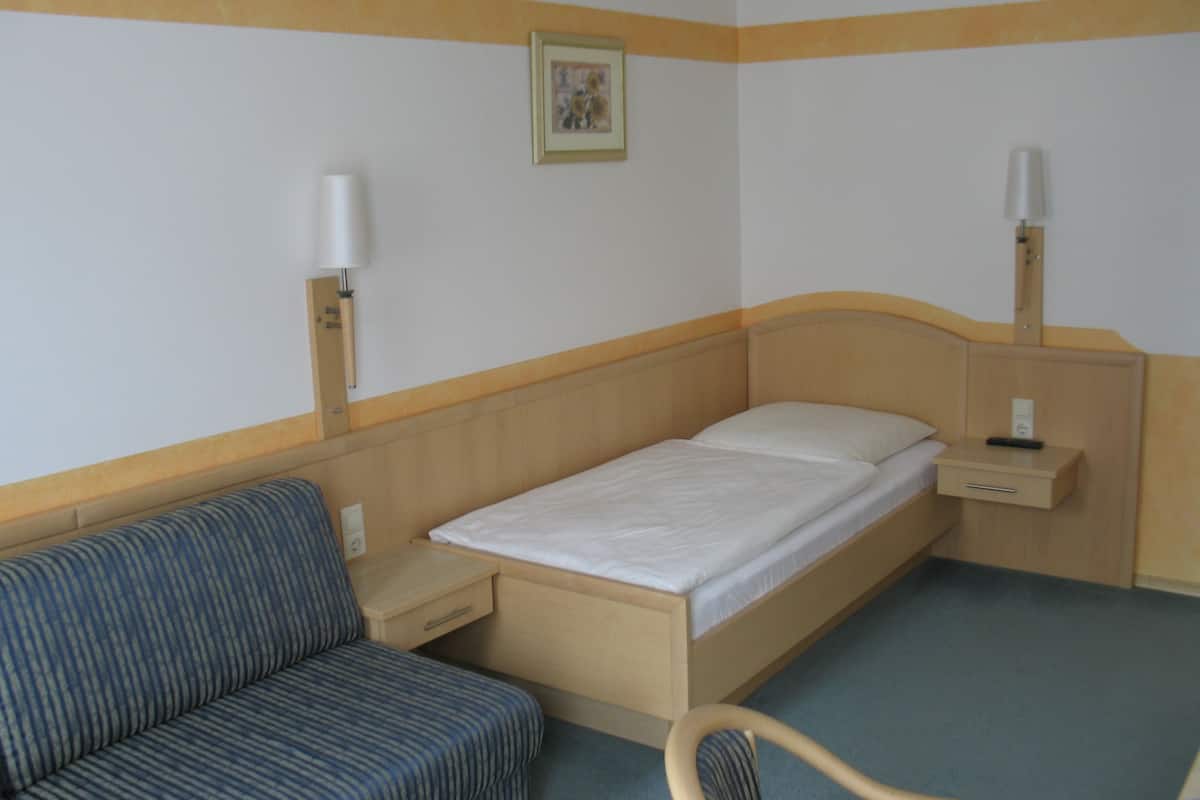 A hotel room with a single bed, a bedside table, a lamp, a chair, and a small table.