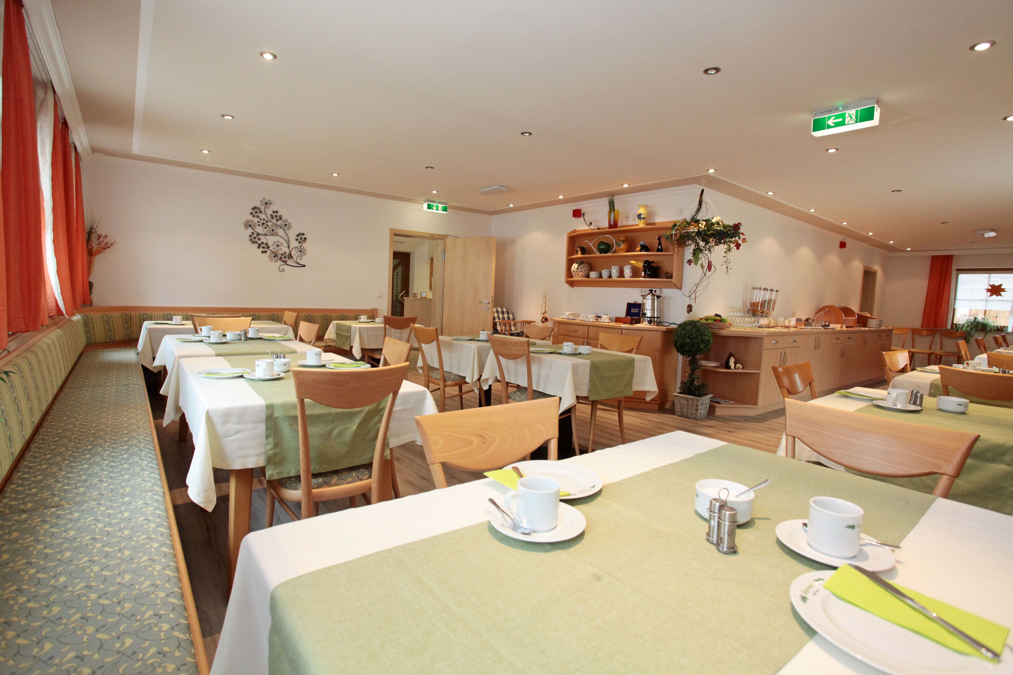 Un espace repas avec plusieurs tables préparées pour le petit-déjeuner, avec des nappes blanches et des serviettes vertes.