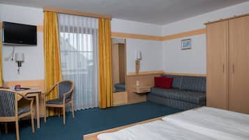 A hotel room with a bed, a desk with a chair, a sofa, a television mounted on the wall, and a wardrobe.