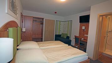 A hotel room with a bed, a desk, a chair, a TV, and a shower.