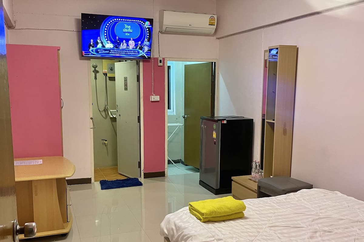 Habitación de hotel con cama, televisor, armario, espejo y zona de ducha.