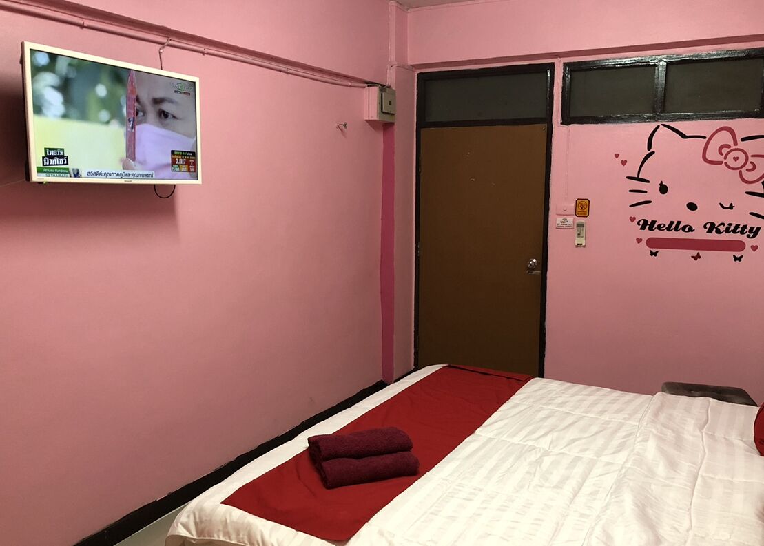 Een roze kamer met een bed, een aan de muur bevestigde televisie en een Hello Kitty decoratie.