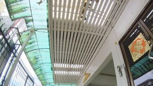 Zona exterior coberta amb sòl de rajola, una furgoneta blanca i una moto aparcades sota una estructura amb teulada de llistons.
