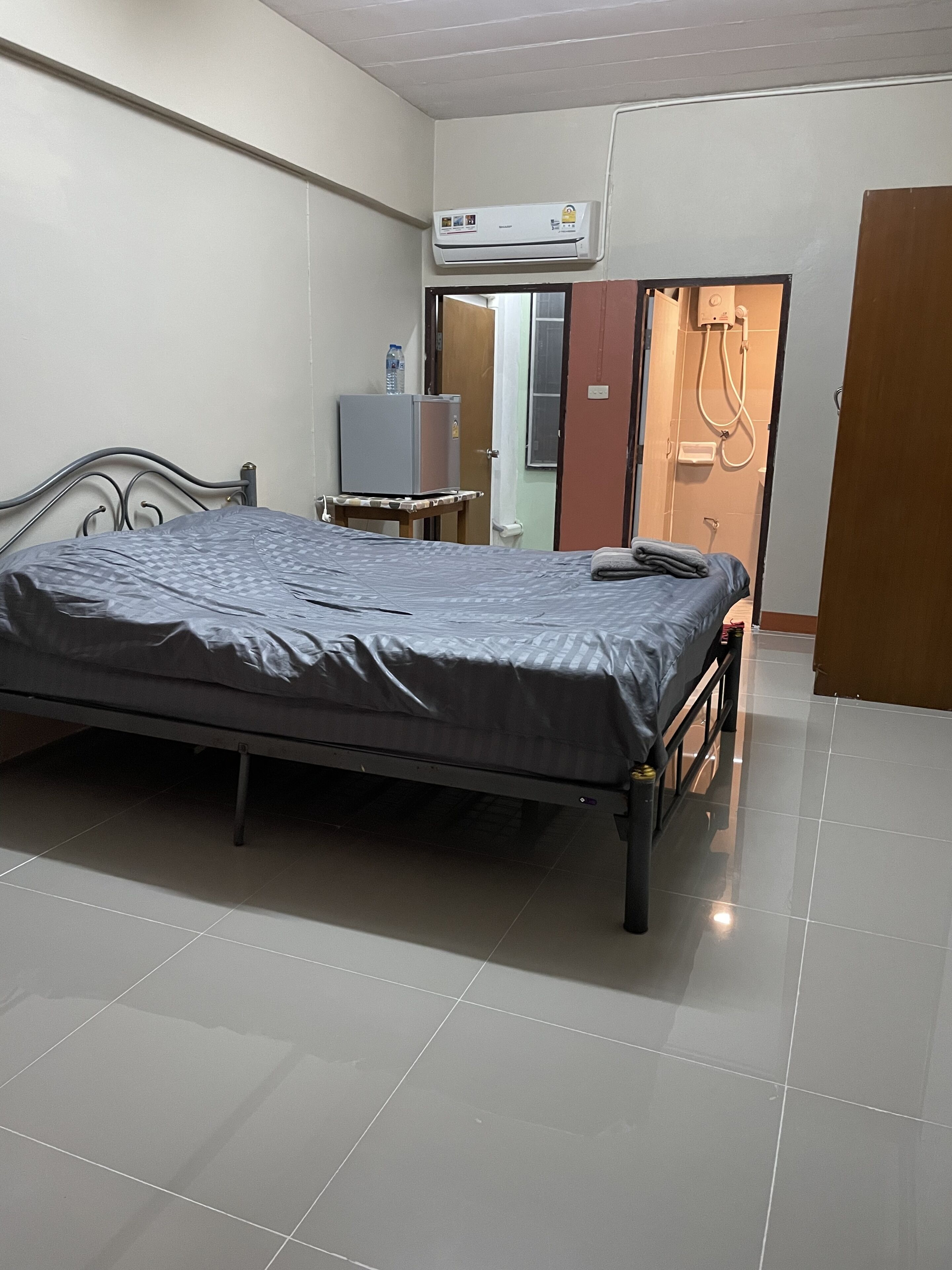 Ein Schlafzimmer mit einem Bett, einem kleinen Tisch, einer Klimaanlage und einer Tür zu einem Badezimmer.