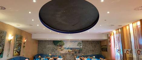 A restaurant with a large circular ceiling feature, stone walls, and blue table settings.