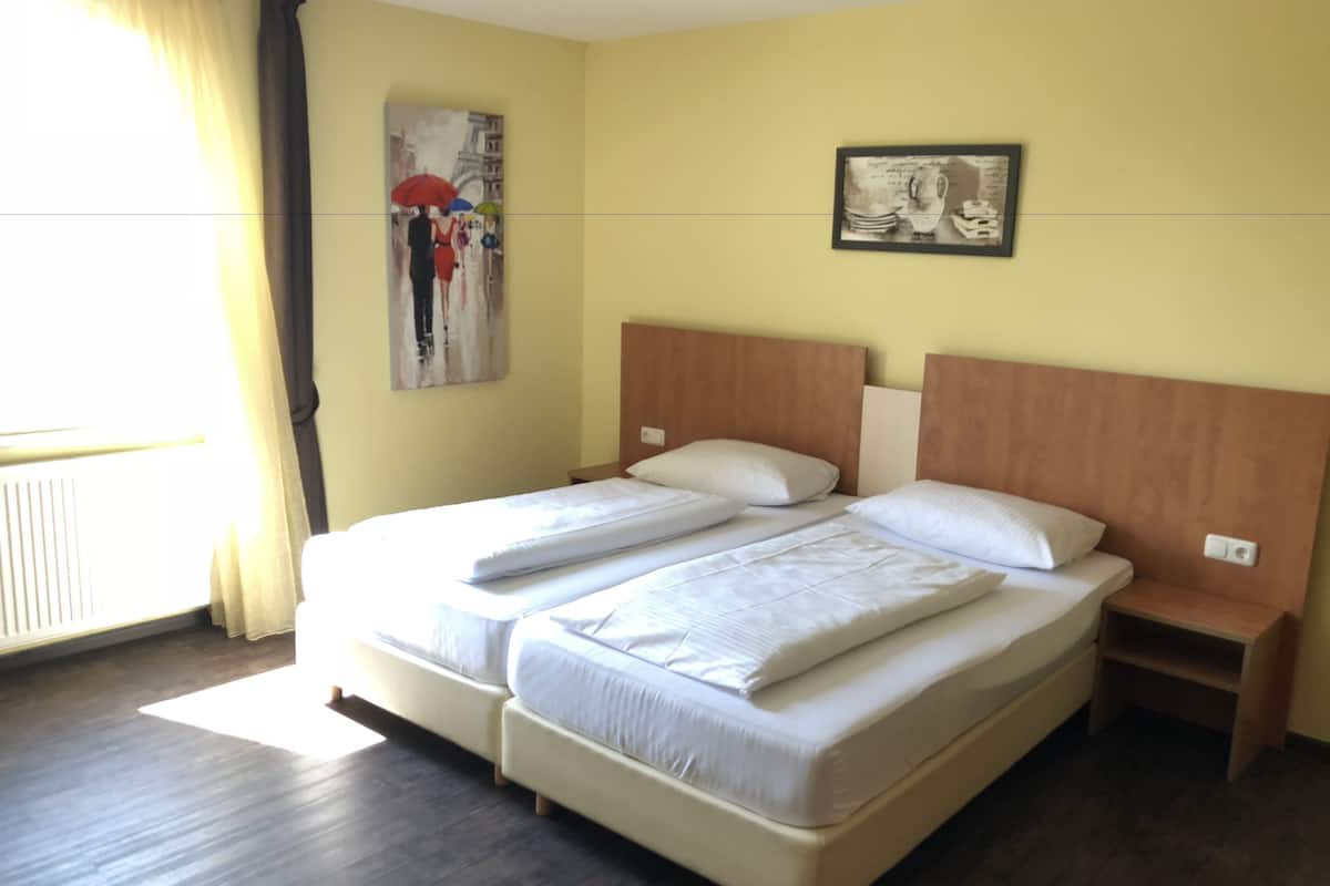 Ein Doppelbett mit Holz Kopfteil, ein Nachttisch, ein Wandbild und ein Fenster mit Vorhängen.