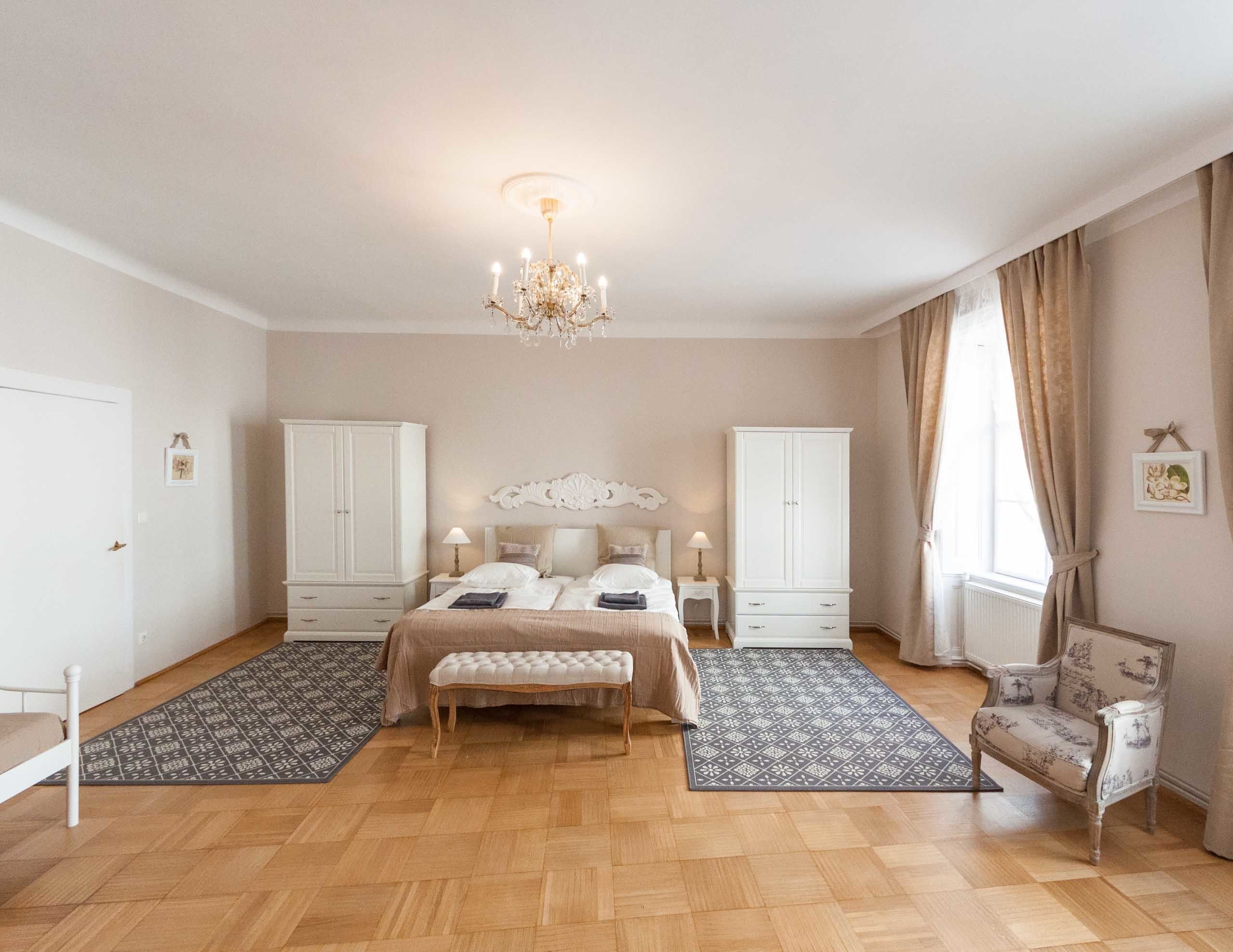 A spacious bedroom with a large bed, two nightstands, a bench, and a chair.