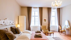 A hotel room with a bed, a desk with a mirror, a chair, a chandelier, and a window with curtains. - ElegantVienna Apartments (Vienna)