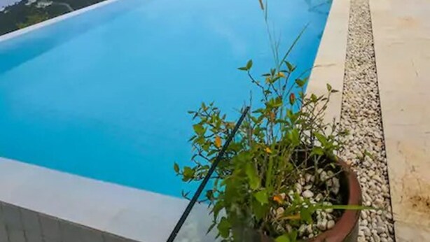 Une magnifique piscine à débordement d’un bleu profond, offrant une vue sur l’océan et les collines.