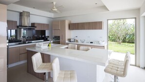 Une cuisine moderne avec un îlot central, des tabourets de bar blancs et une vue sur un jardin grâce à une grande fenêtre.