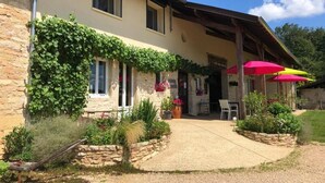A two-story building with a stone facade, a covered patio area, and outdoor seating with umbrellas. - La Ferme du Bonheur (Arbigny)