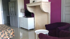 A modern living room with a beige sofa, a small white table, and a purple armchair. A white cabinet with a television and a lamp is against the wall. - La Ferme du Bonheur (Arbigny)