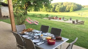 An outdoor dining area with a table set for a meal, surrounded by chairs, and a view of a grassy field and trees in the background. - La Ferme du Bonheur (Arbigny)