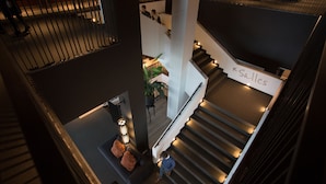 A multi-level interior with a staircase, a sign reading "Salles," and a seating area with a plant.