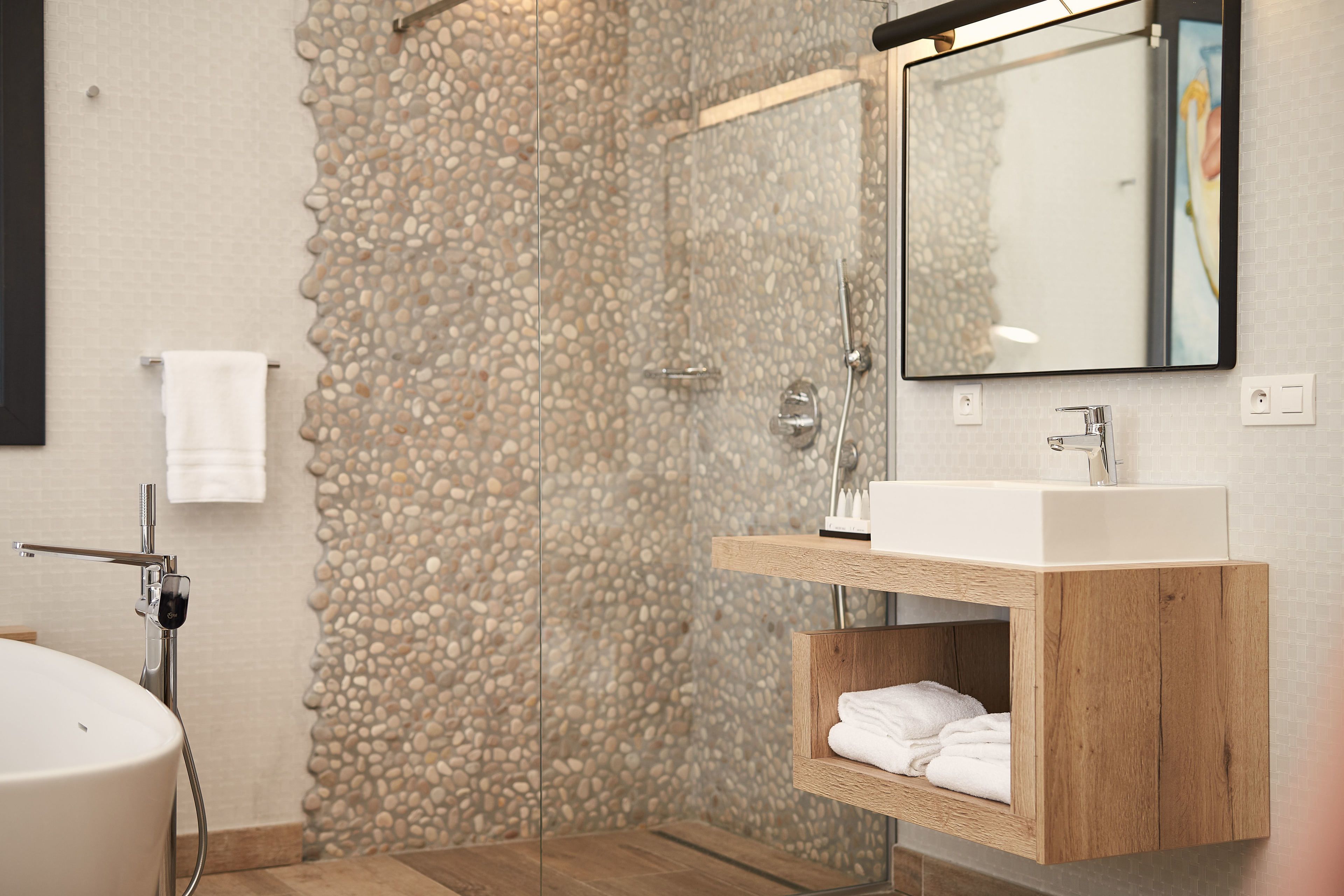 A bathroom with a stone wall, a wooden vanity, a white sink, and a glass shower enclosure.