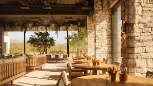 A covered outdoor seating area with stone walls, wooden furniture, and potted plants.