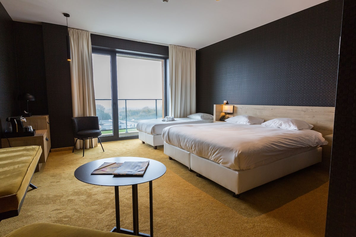 Habitación de hotel con dos camas, un escritorio, una silla y un ventanal grande.