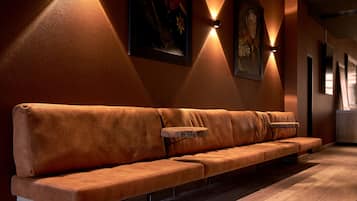 A long, leather sofa with a wooden side table against a wall with two wall-mounted lights.