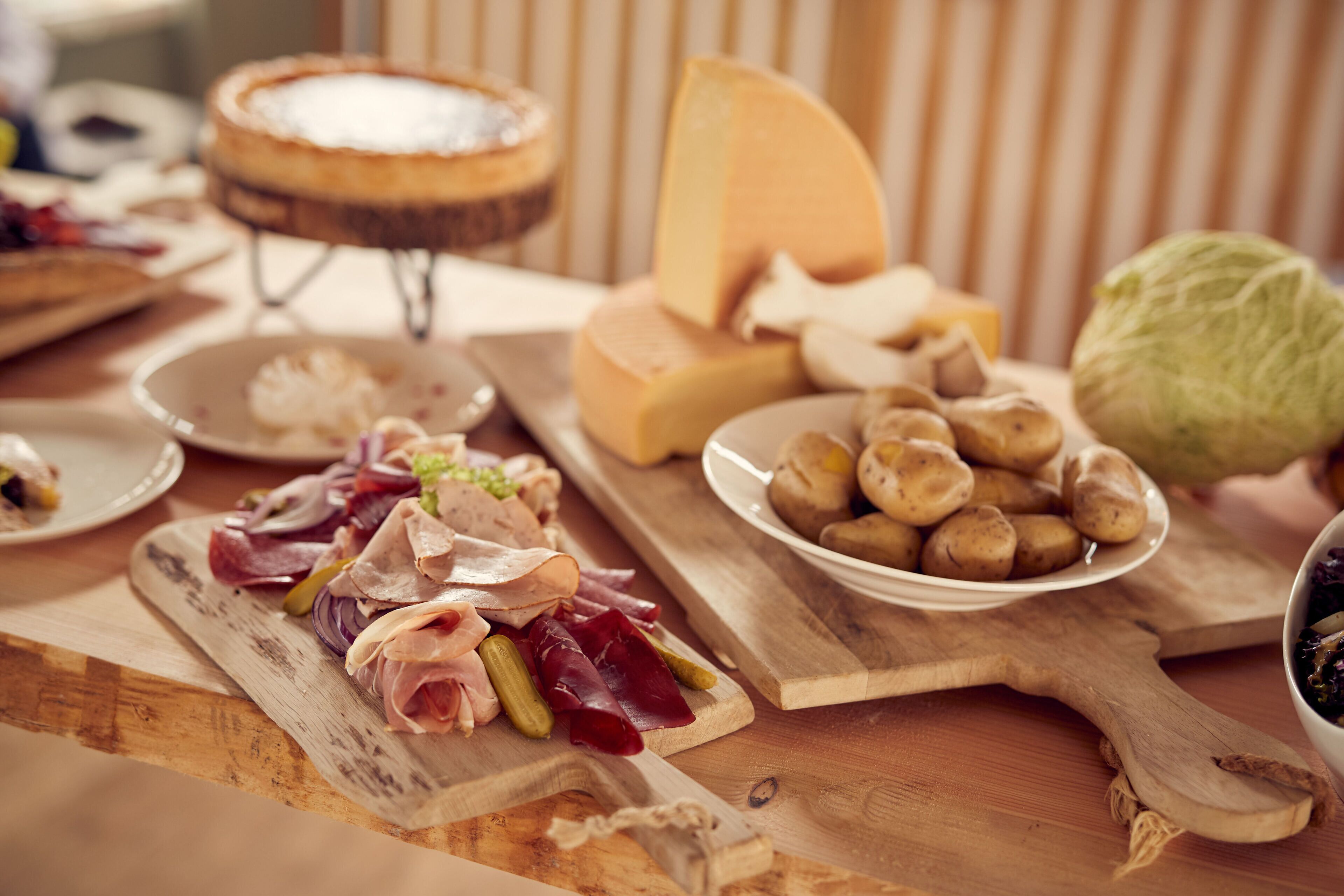 A wooden cutting board with various cheeses, cured meats, and pickles.
