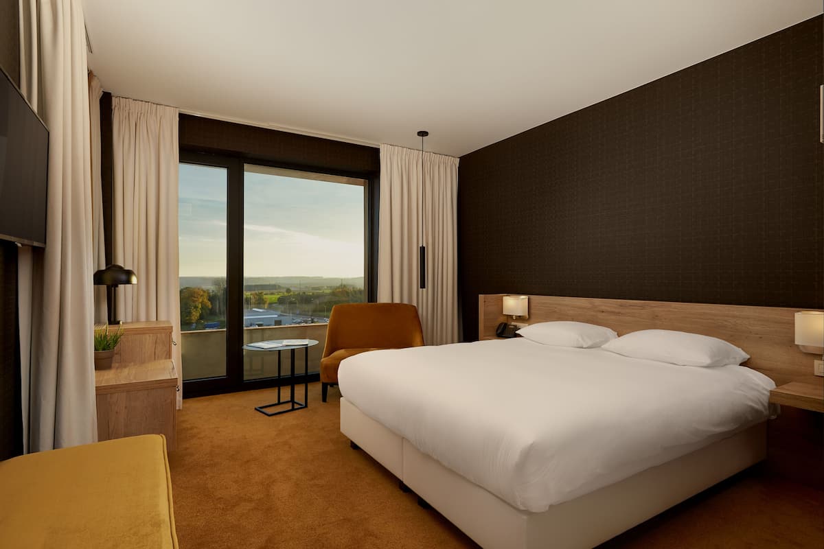 Habitación de hotel con una cama grande, una silla, una mesita y vistas al exterior.