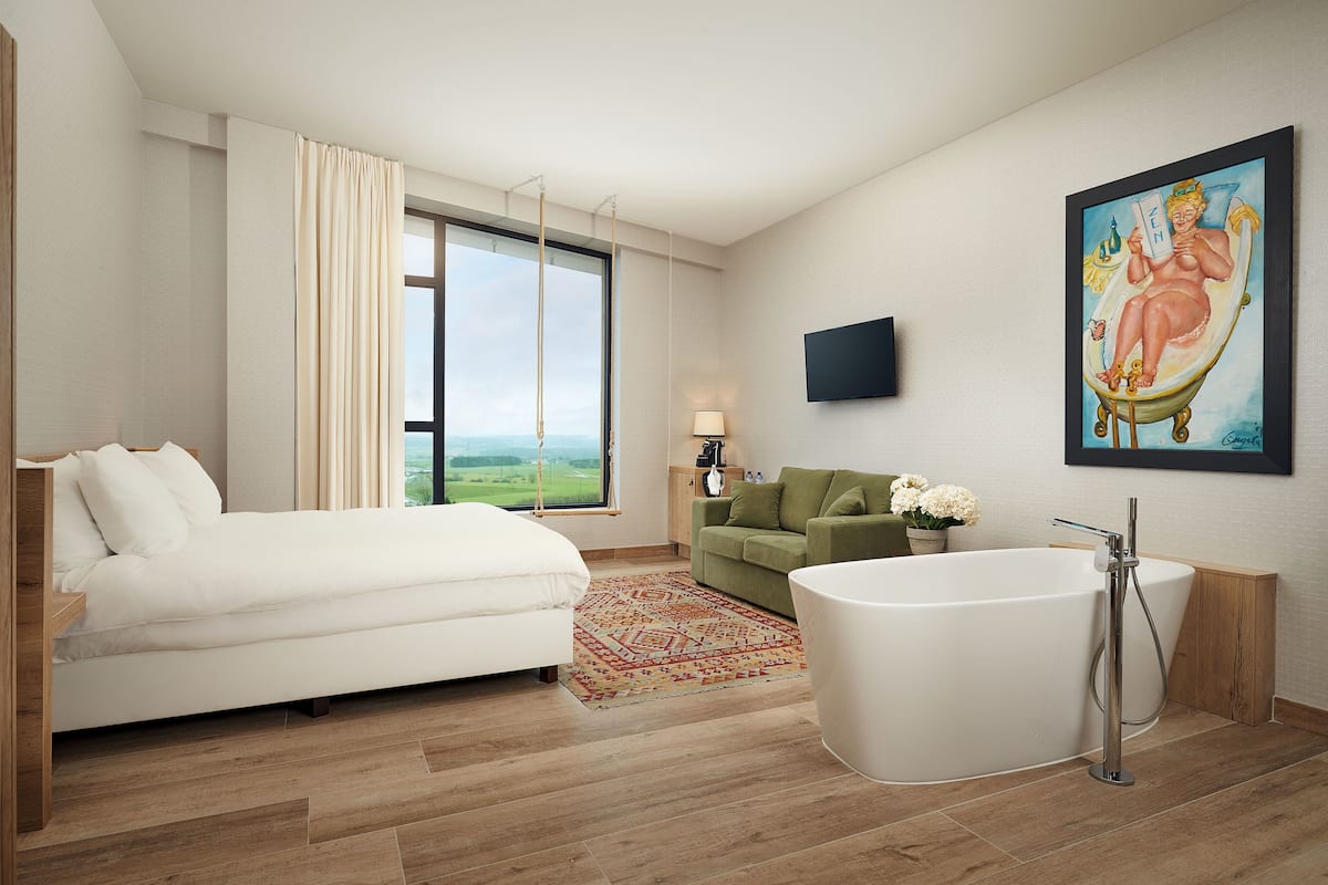 Un dormitorio moderno con una cama grande, un sofá verde, una bañera y un cuadro en la pared.