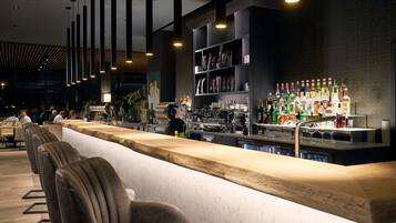 Zona de bar con una barra larga, taburetes y una variedad de botellas y vasos.
