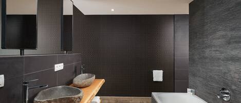 Un baño moderno con una bañera grande, dos lavamanos de piedra y un mueble de tocador de madera.