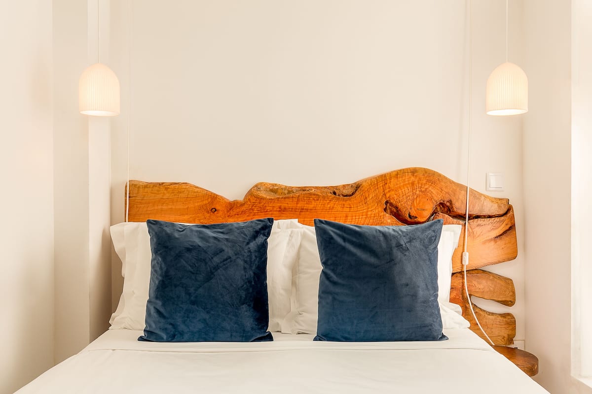Ein Bett mit hölzernem Kopfteil, zwei Kissen und zwei Pendelleuchten.
