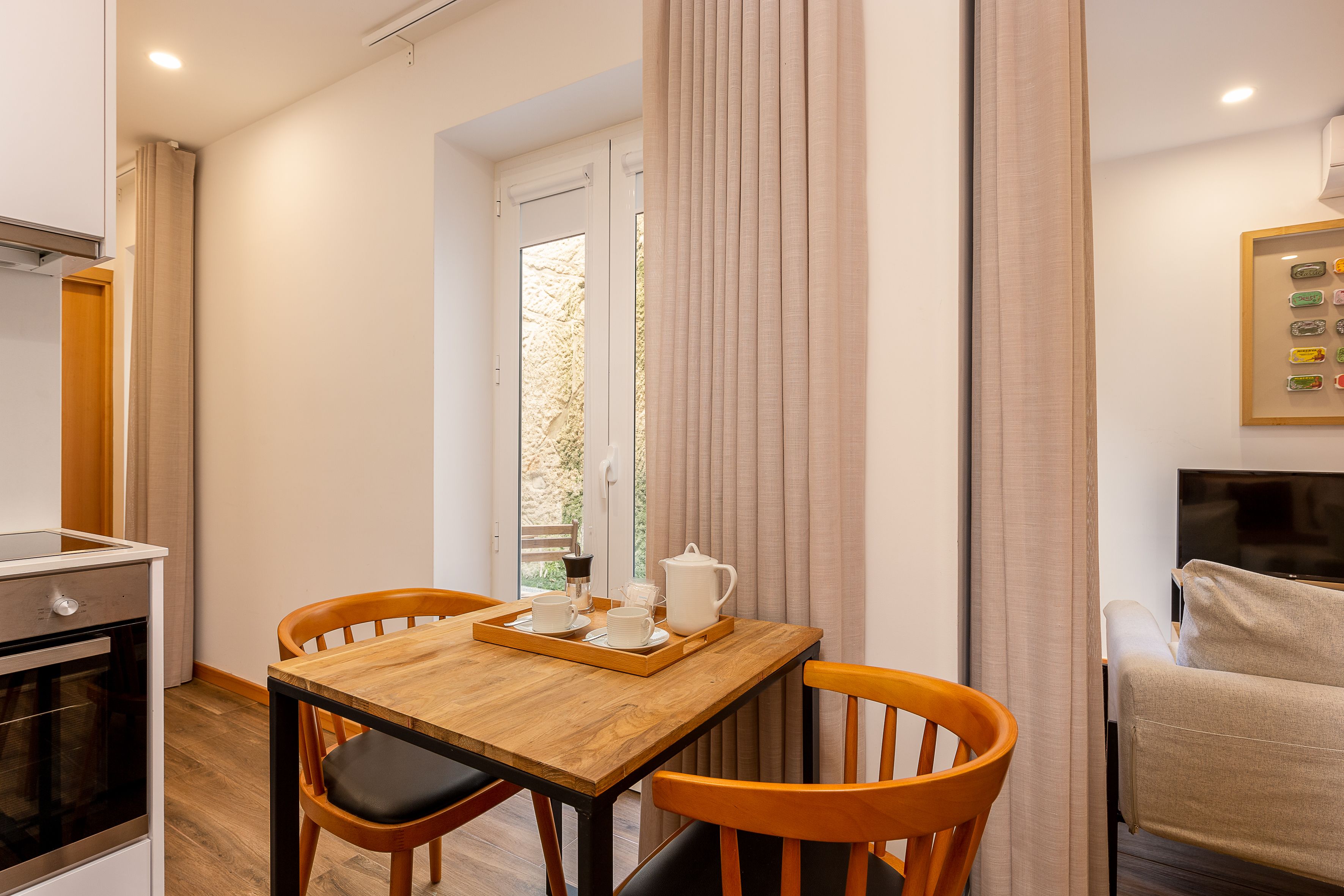 Un coin repas avec une table en bois, deux chaises, un plateau avec une théière et des tasses, et un téléviseur fixé au mur.
